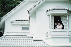 A man and Dalmatian dog enjoying a view from a white house's open window.