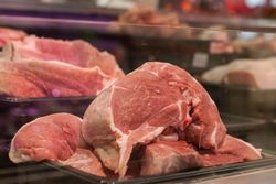 Close-up of fresh raw pork cuts on display in a glass case at a market.