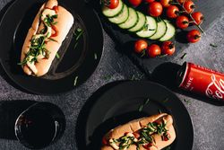 Savor gourmet hot dogs topped with fresh vegetables, served with a refreshing cola.