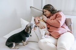 A mother feeds her newborn baby while a small dog watches attentively on the bed.