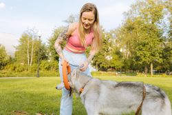 A tattooed woman enjoying playtime with her Siberian Husky in a park.