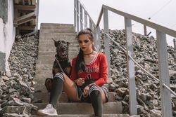 Woman in urban attire sits on stairs with a Doberman, creating a moody vibe.