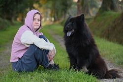 A young woman in a hoodie sitting with a large black dog on a grassy path.